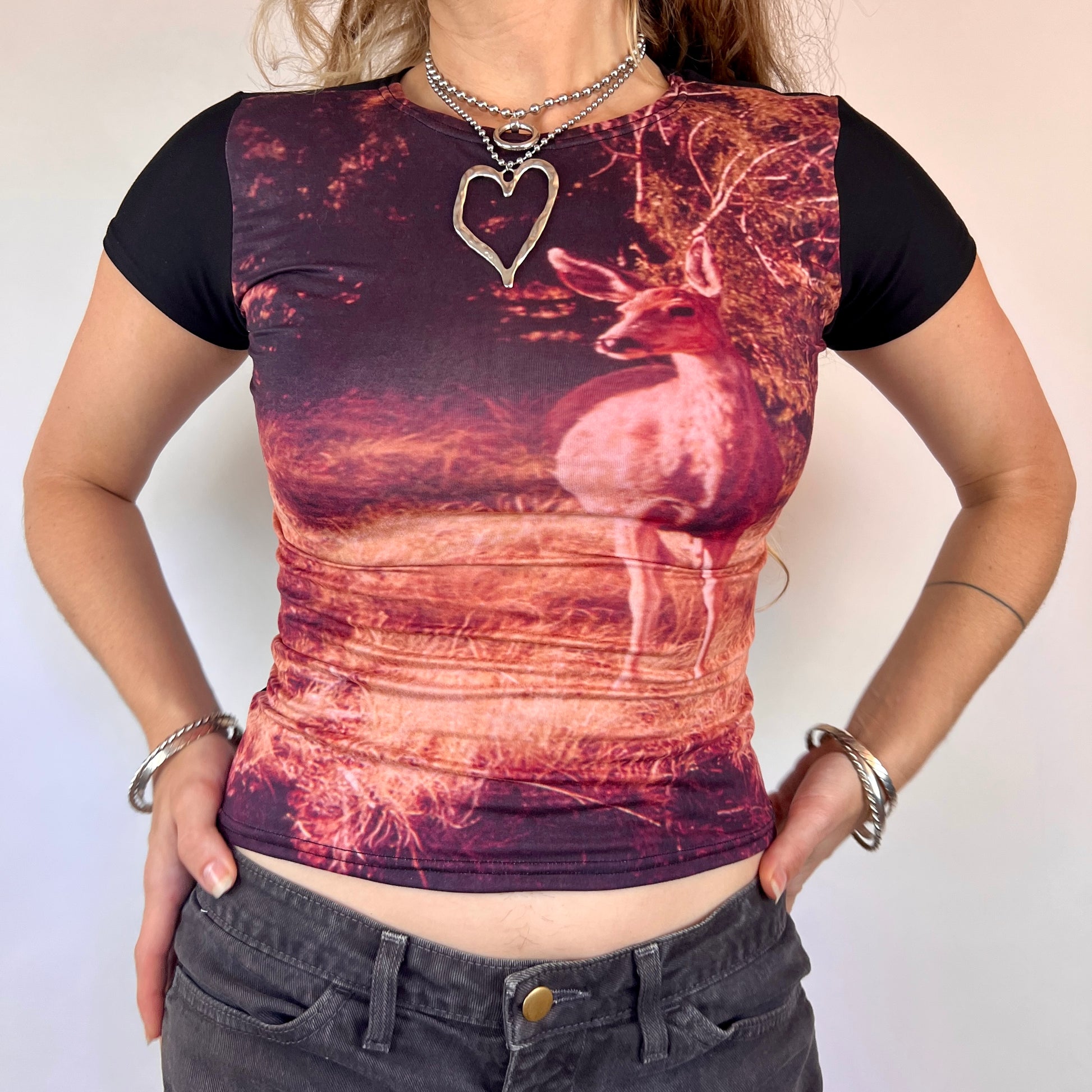 Person wearing a black t-shirt with a deer design and heart pendant necklace.