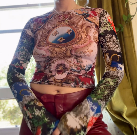 Person wearing a colorful, patterned long-sleeve top with a rococo design on front and long sleeves with tiger and bamboo print.